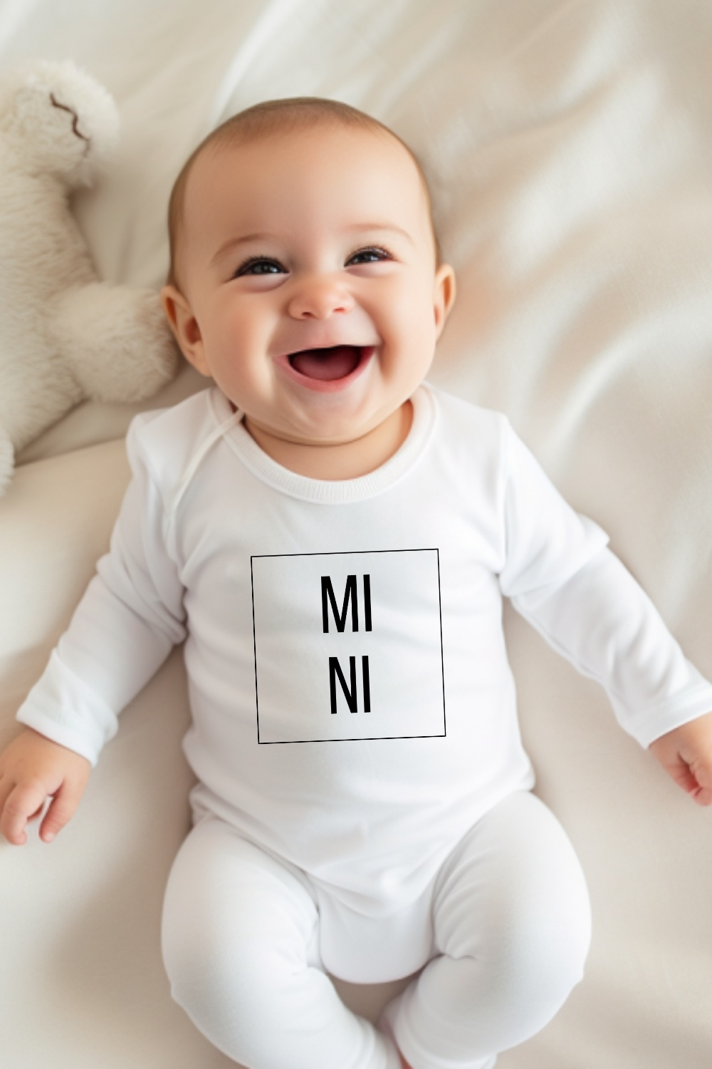 Lächendes Baby im kuscheligen weißen Babybody mit "MINI" Schriftzug, weiche bequeme Babykleidung.