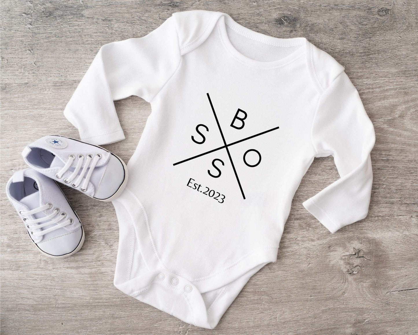 Babybody with graphic design and baby shoes on wooden surface.