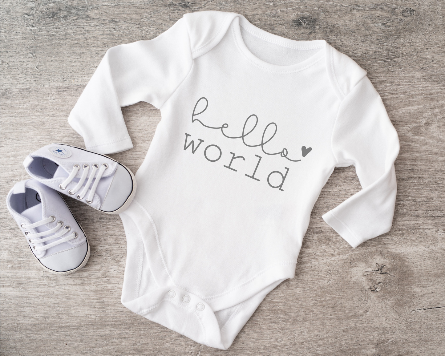 White babybody with "hello world" text and matching shoes on wooden surface.