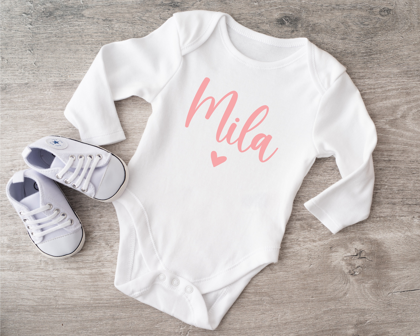 Weicher Babybody mit Schriftzug Mila und passenden Babyschuhen auf Holz.