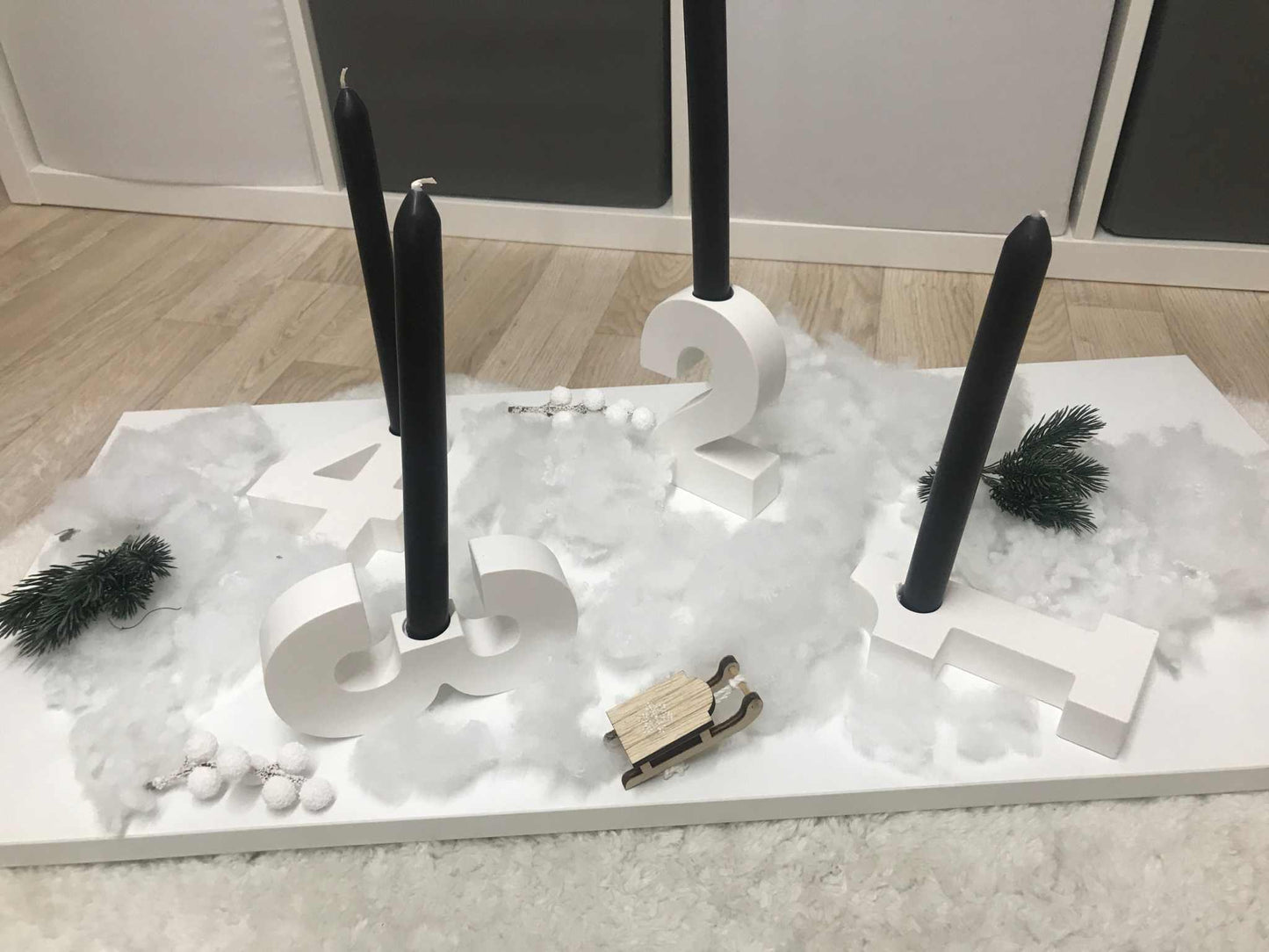 Minimalistischer Raysin-Adventskranz in Weiß mit Zahlen und schwarzen Stabkerzenhalterungen.