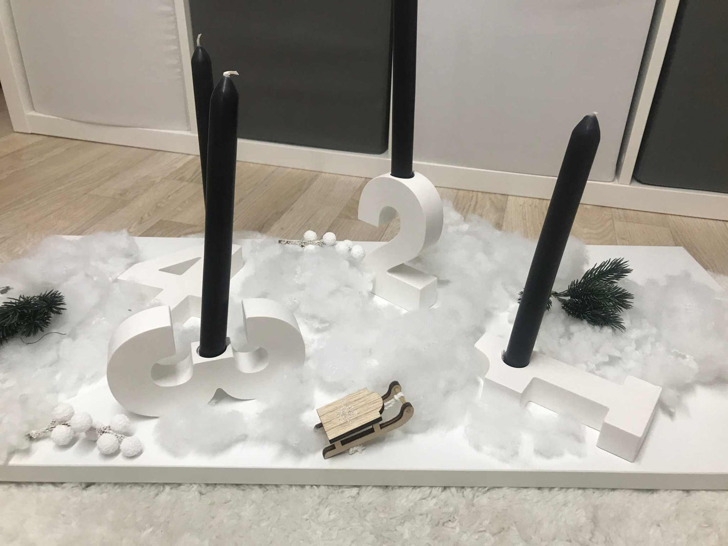 Minimalistischer Adventskranz mit weißen Raysin-Zahlen und Haltern für Stabkerzen, dekoriert auf einem weißen Untergrund.