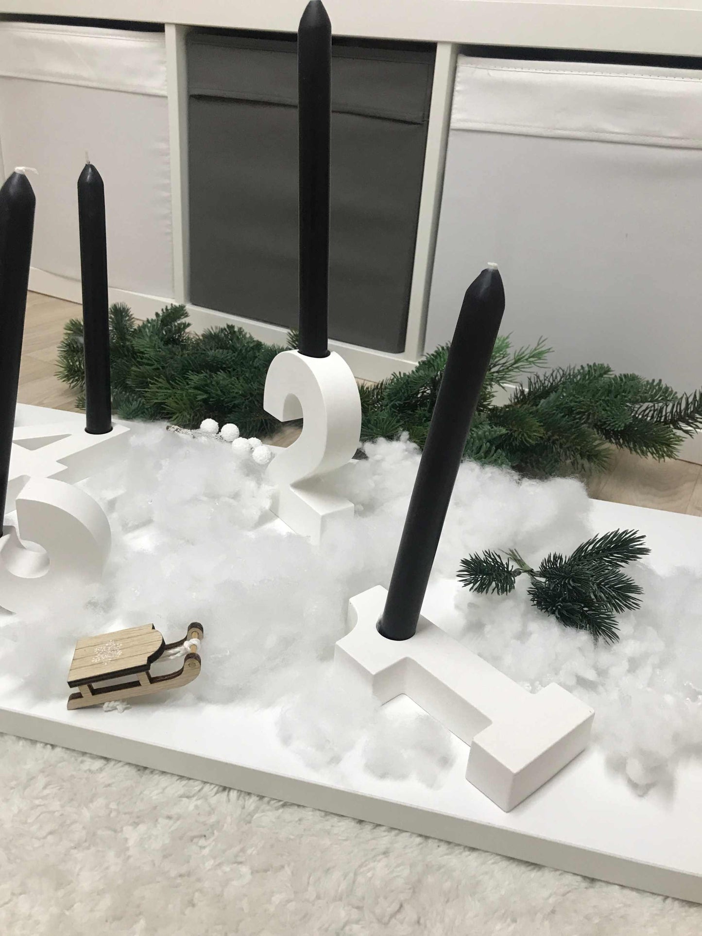 Minimalistischer Adventskranz aus Raysin mit schwarzen Stabkerzen und Zahlen in Weiß auf einem Tisch.