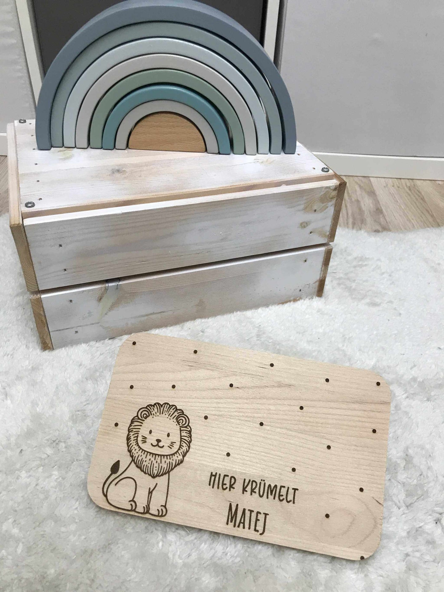 Holz Frühstücksbrettchen mit Löwenmotiv auf Teppich, dekoriert mit buntem Holzregenbogen im Hintergrund.