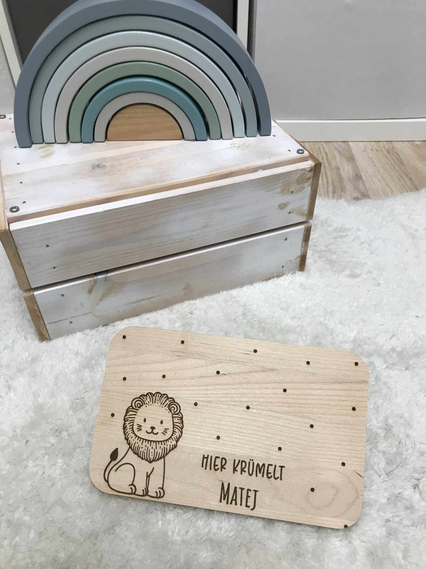 Löwenmotiv Frühstücksbrettchen aus Holz auf weichem Teppich neben Spielzeugbogen.
