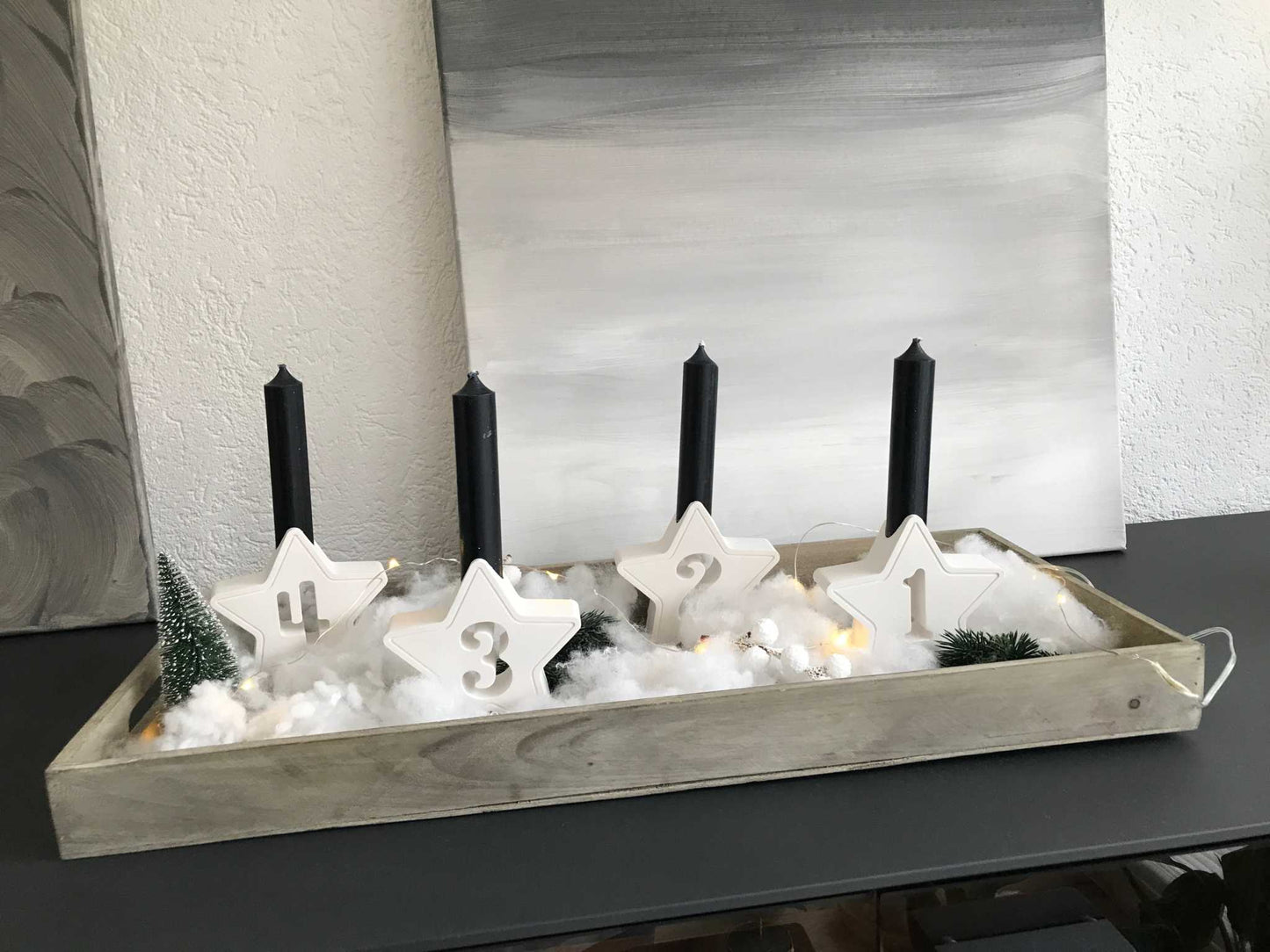 Minimalistischer Adventskranz mit weißen Kerzenhaltern aus Raysin, dekoriert mit Sternen und Adventszahlen.