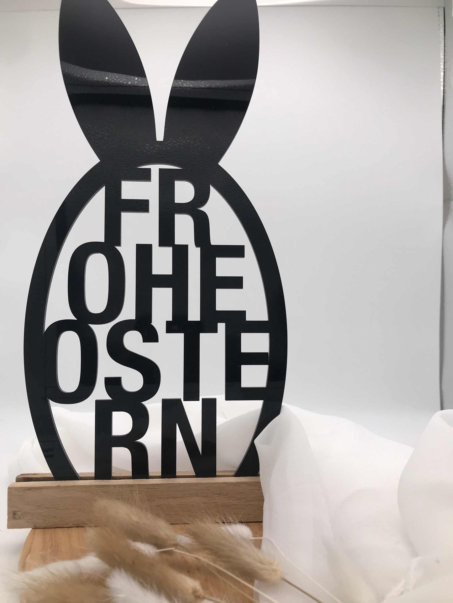 Osterdekoration mit "Frohe Ostern" Schriftzug aus Acryl und Holzklötzchen auf weißem Hintergrund.