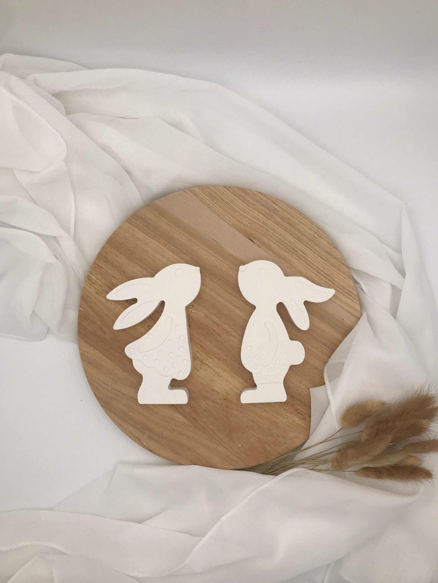 Osterdekoration mit zwei weißen Osterhasen aus Raysin auf Holzplatte.