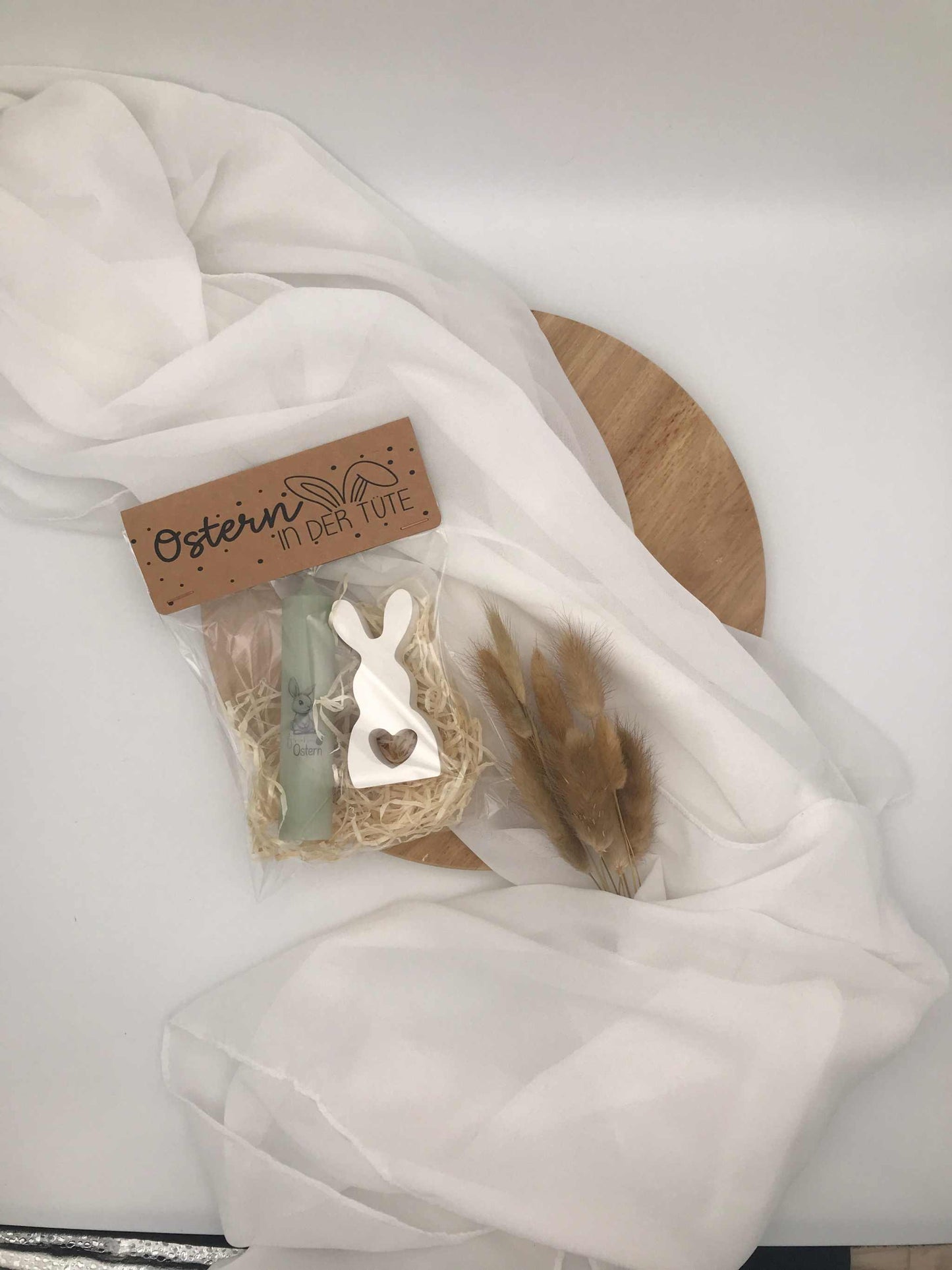 Ostergeschenkset mit Kerze und handgefertigtem Keramikhasen, dekorativ verpackt auf Holzteller mit weißem Stoff.