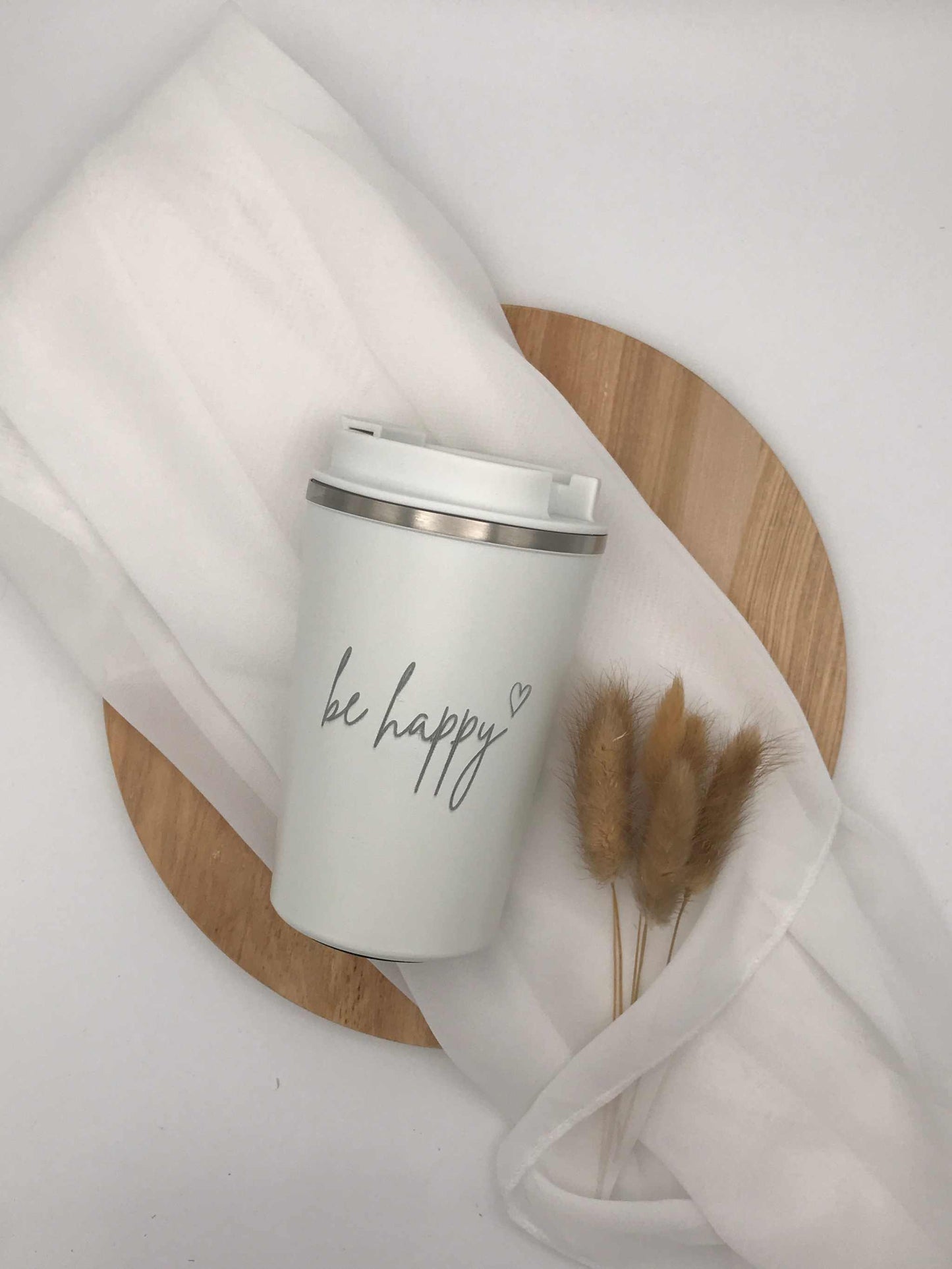 Doppelwandiger Thermobecher mit "be happy" Gravur auf Holz und Stoffhintergrund.