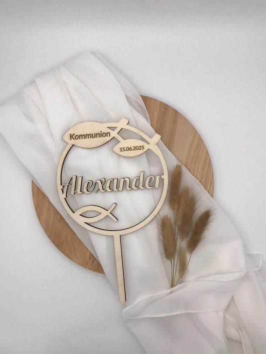 Caketopper aus Holz zur Taufe oder Kommunion, personalisiert mit Namen und Datum, auf weißem Stoff drapiert.