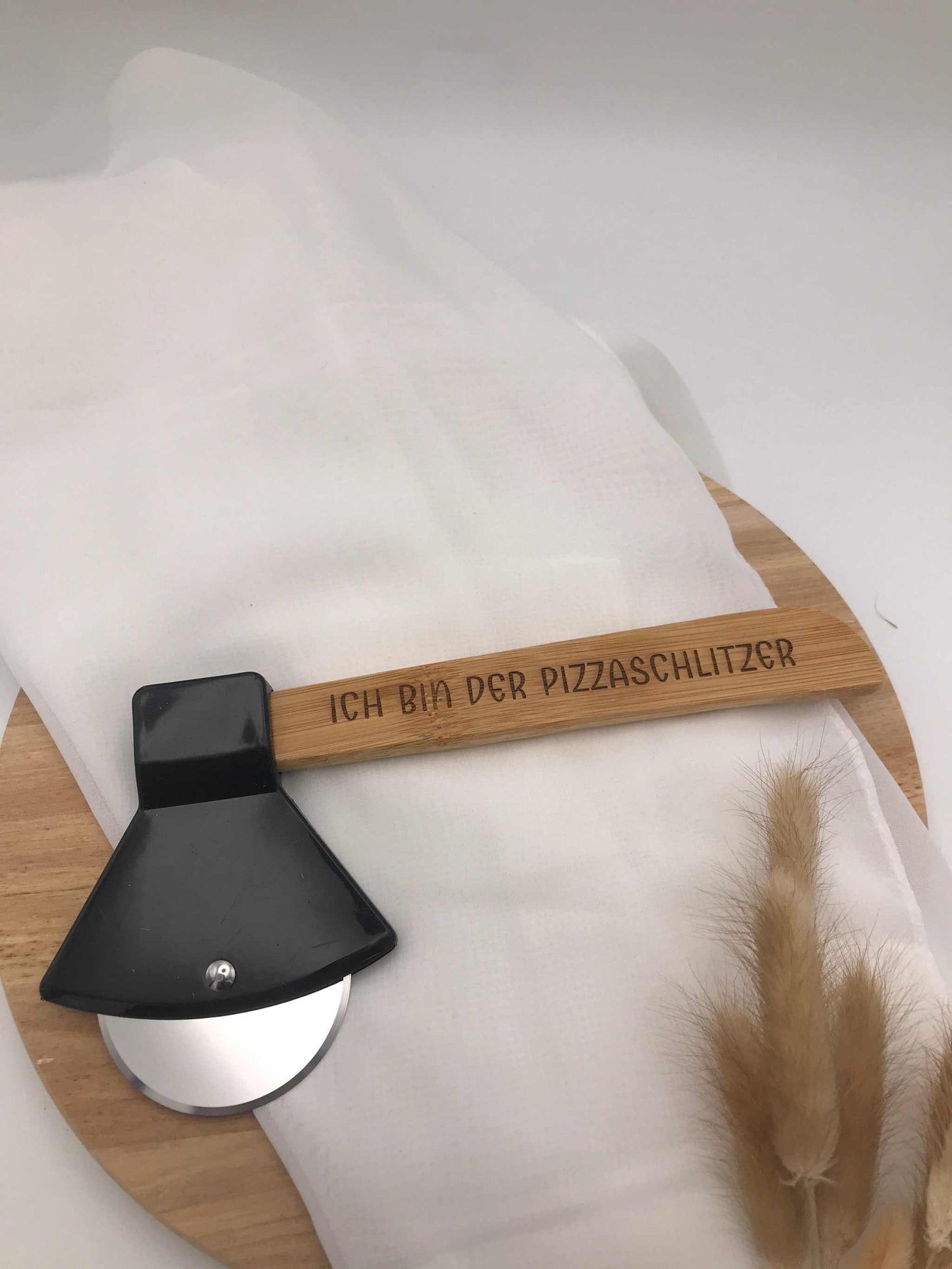 Pizzaschneider in Beilform mit Gravur „Ich bin der Pizzaschlitzer“ aus Edelstahl und Bambusgriff auf Holzbrett