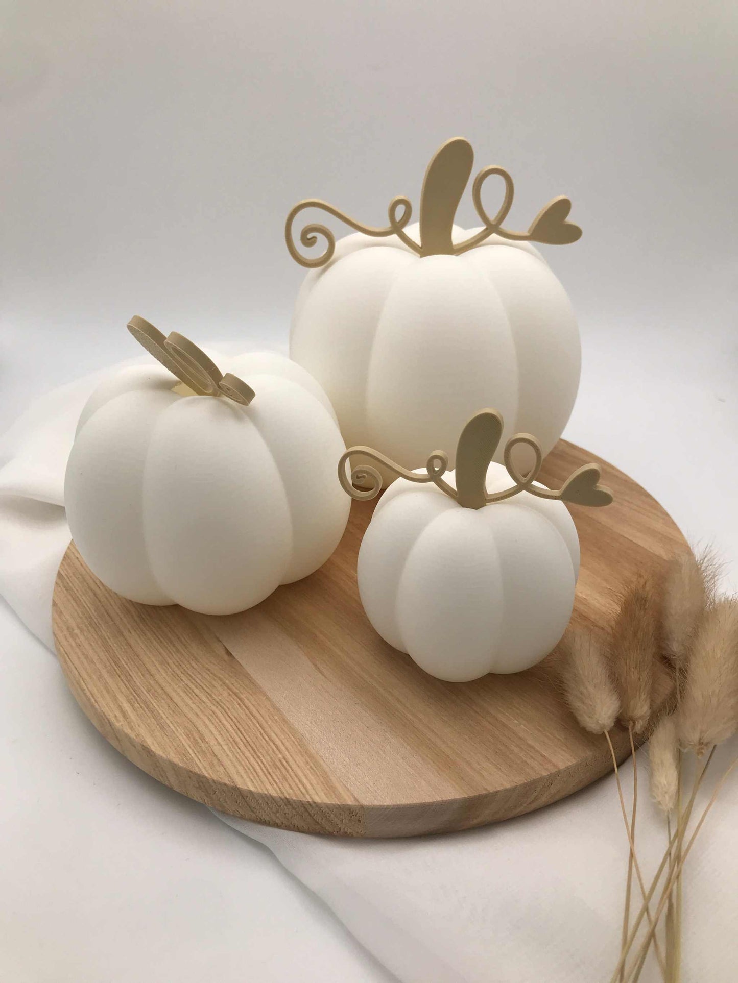 weiße Dekokürbisse aus umweltfreundlichem PLA 3D-Druck in drei Größen mit goldfarbenen Stielen und LED-Teelicht, auf Holzplatte dekoriert, herbstliche Dekoidee