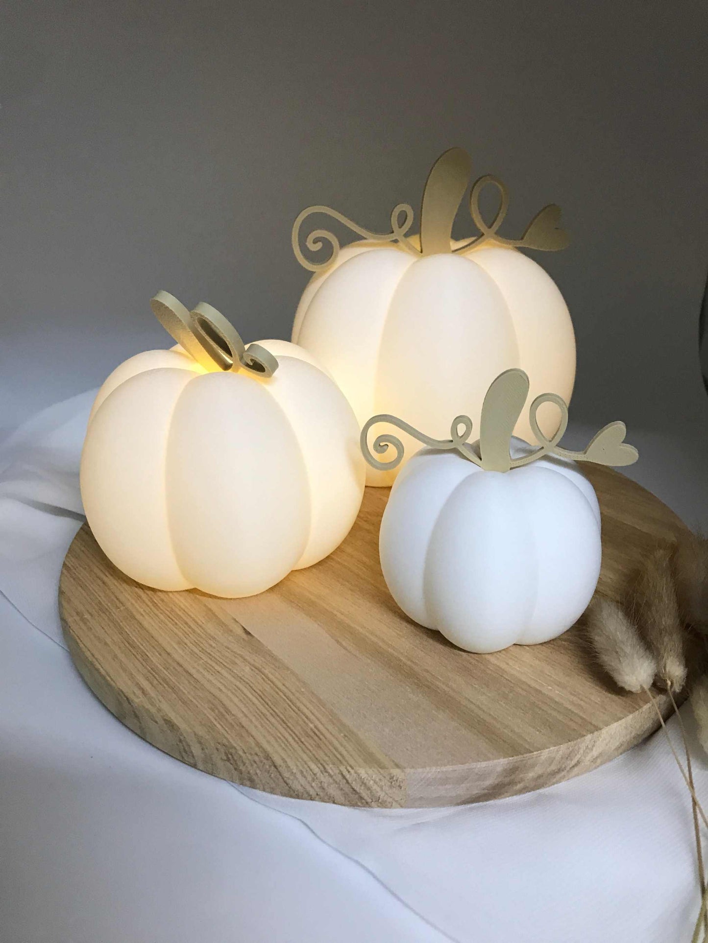 Handgefertigte Dekokürbisse aus PLA 3D-Druck in verschiedenen Größen mit warm leuchtenden LED-Teelichtern auf Holztablett