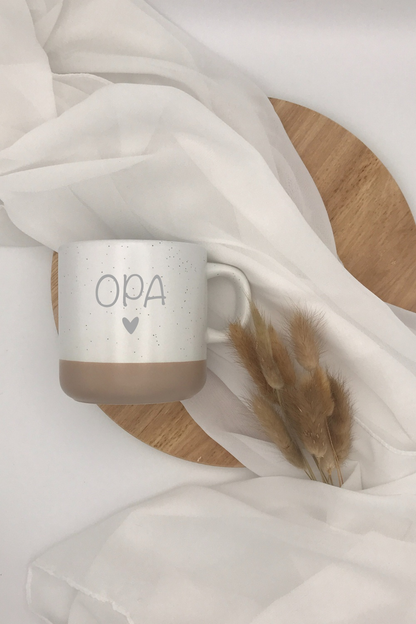 Keramiktasse "Opa" in Grau und Beige mit Herzdekoration auf Holzhintergrund.