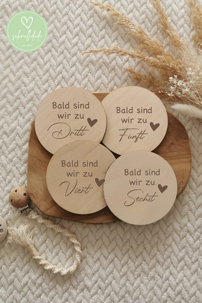 Meilensteinscheiben aus Holz zur Schwangerschaftsankündigung auf Tablett mit natürlichem Hintergrund.