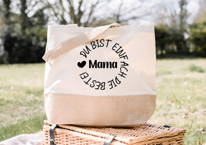 Personalisierte Jutetasche mit Aufschrift "Du bist einfach die Beste, Mama" auf einem Picknickkorb im Freien.