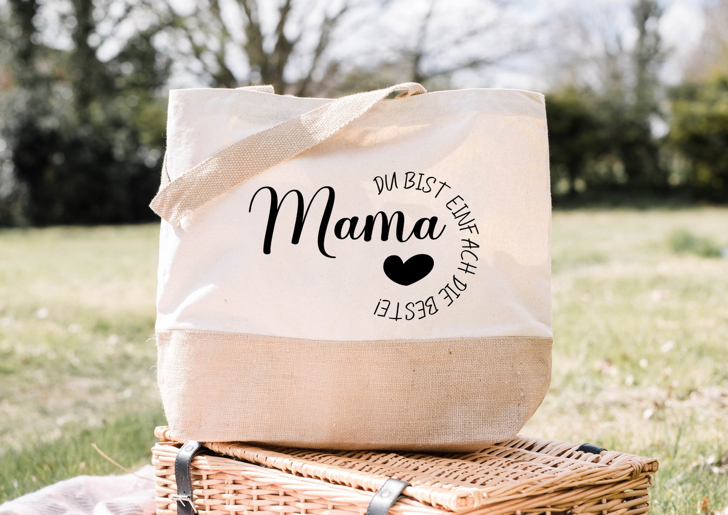 Personalisierte Jutetasche mit Aufschrift "Mama, du bist einfach die Beste", im Freien auf einem Picknickkorb.