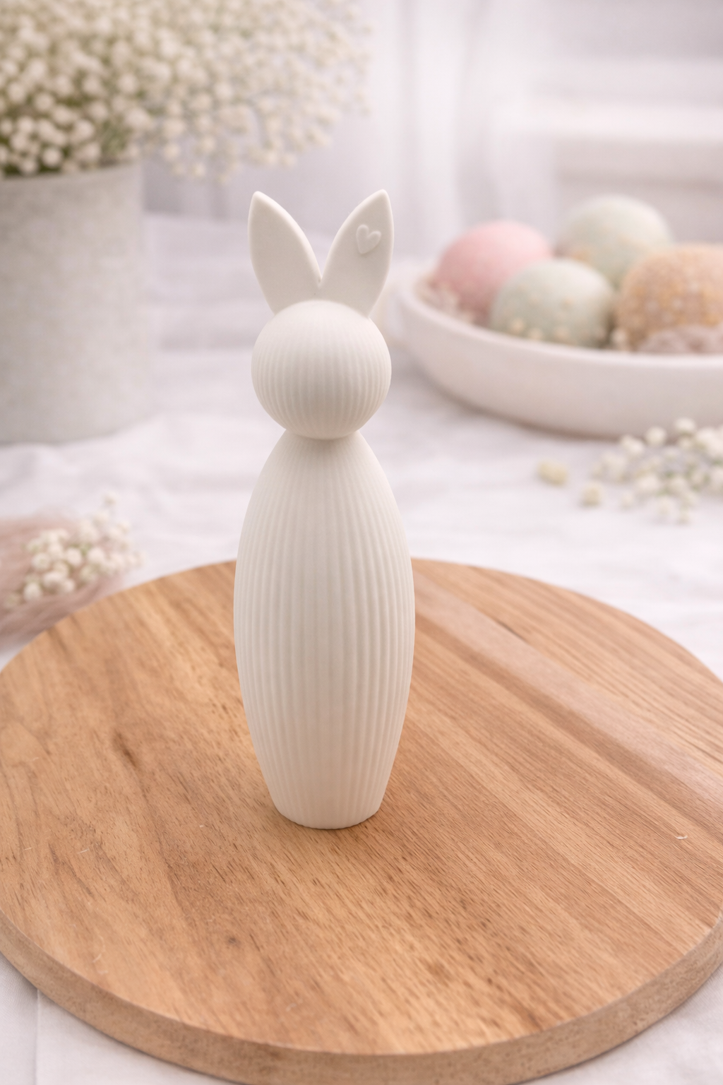 Weißer Osterhase aus PLA mit feiner Rillenstruktur auf Holzbrett, minimalistische Frühlingsdekoration mit zarten Trockenblumen im Hintergrund