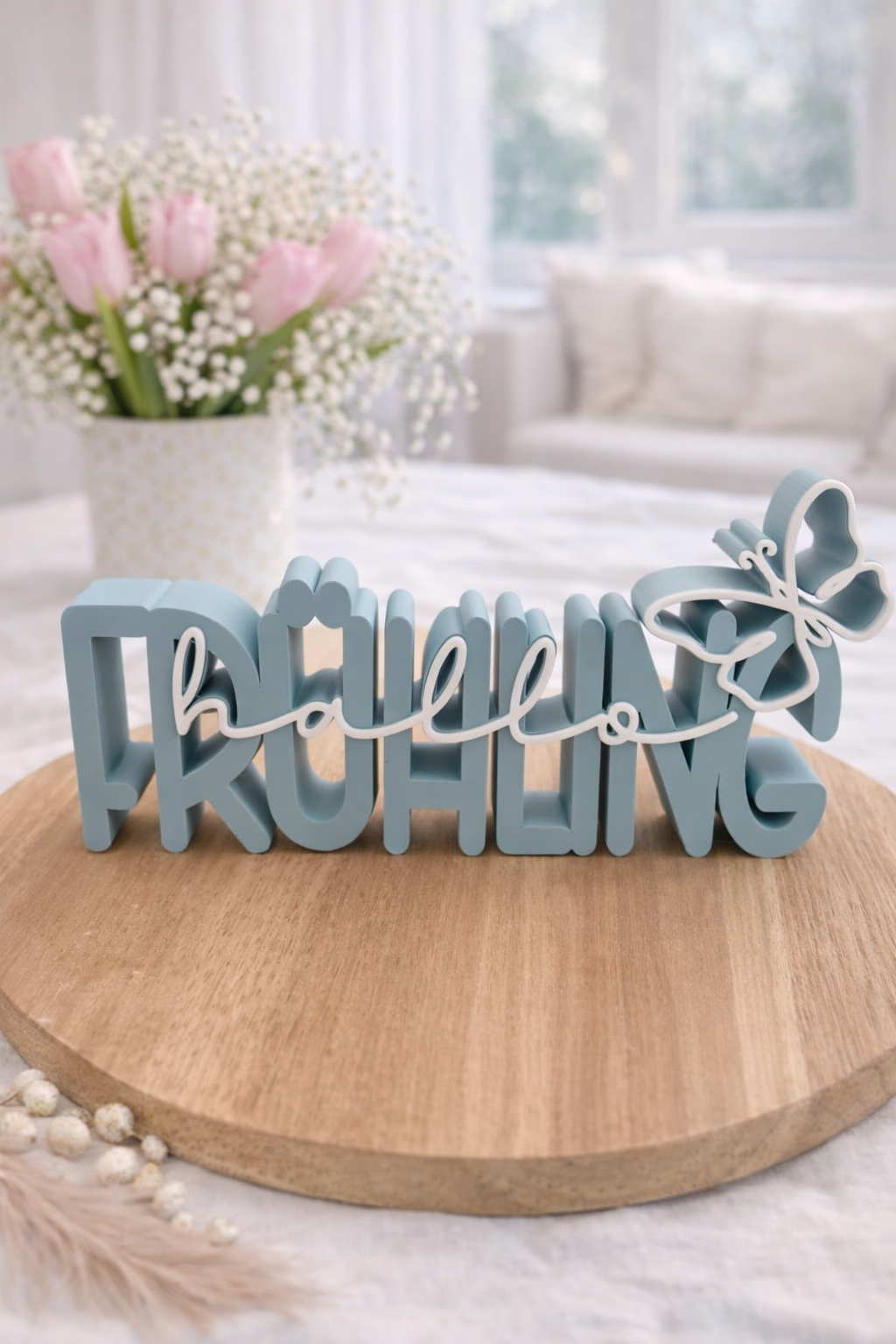 Tischdeko Frühling: ‚Hallo Frühling‘ Schriftzug in Rosé mit Blumen im Hintergrund