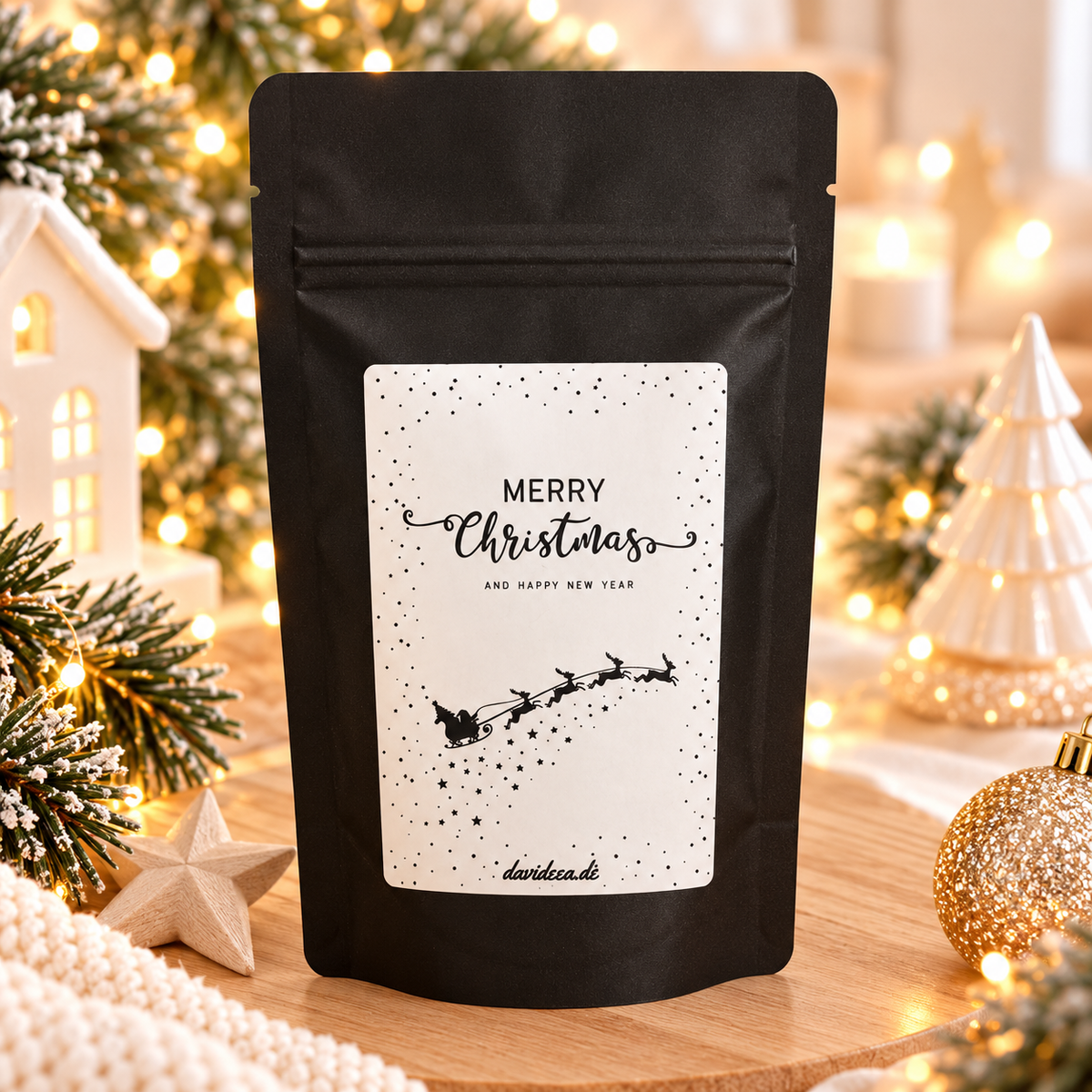 Kaffee in schwarzer, matter Geschenktüte mit weißem Weihnachtsaufkleber „Merry Christmas“ und Schlittenmotiv
