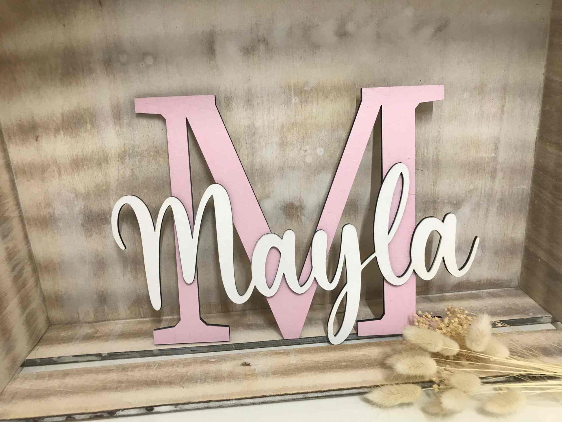 Personalisierbares Türschild für Kinderzimmer mit großem rosa Buchstaben "M" und weißem Schriftzug "Mayla" aus Sperrholz.