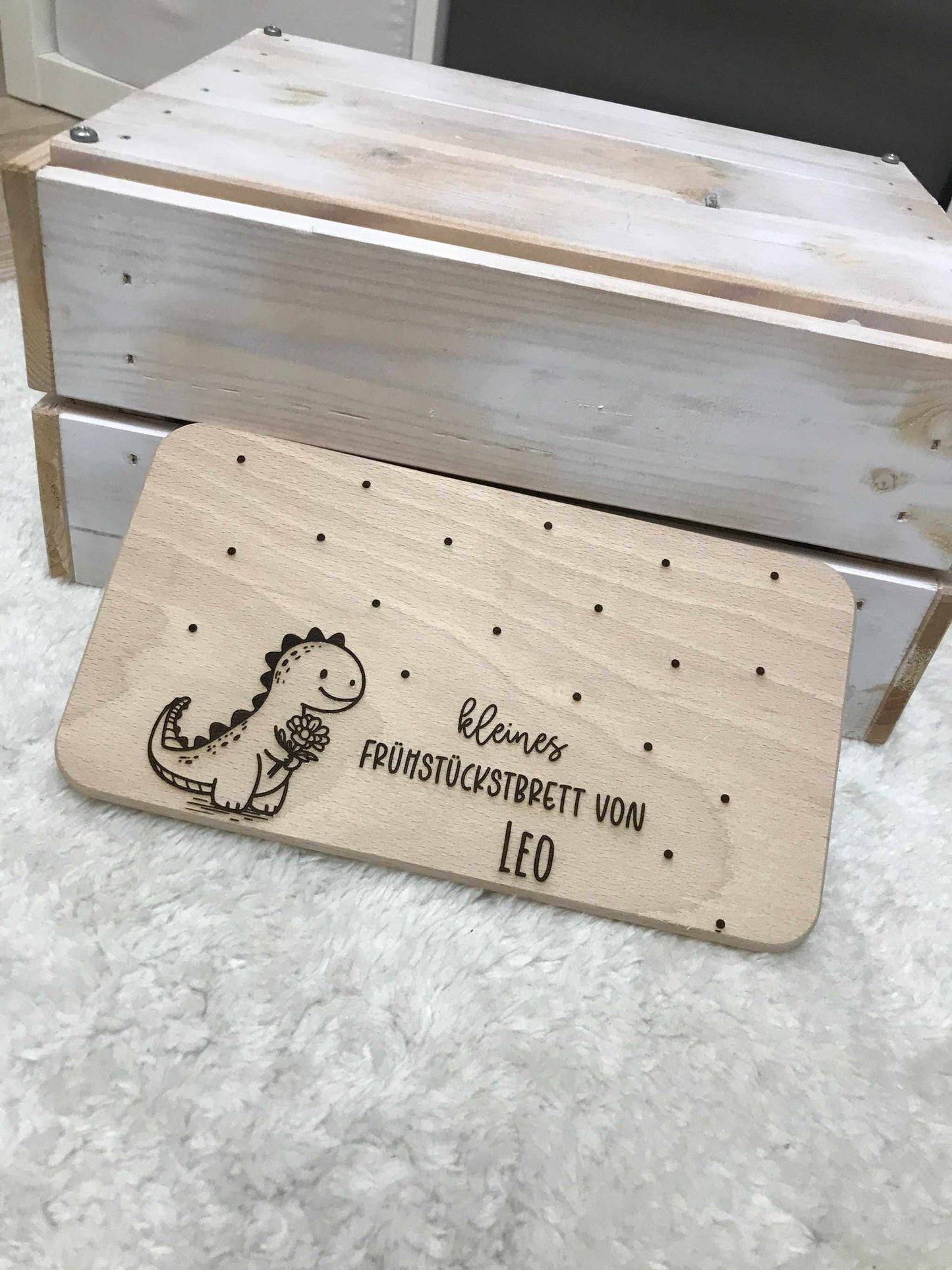 Holz-Frühstücksbrettchen mit Dinosaurier-Design und Gravur "Kleines Frühstücksbrett von Leo" auf Teppich.