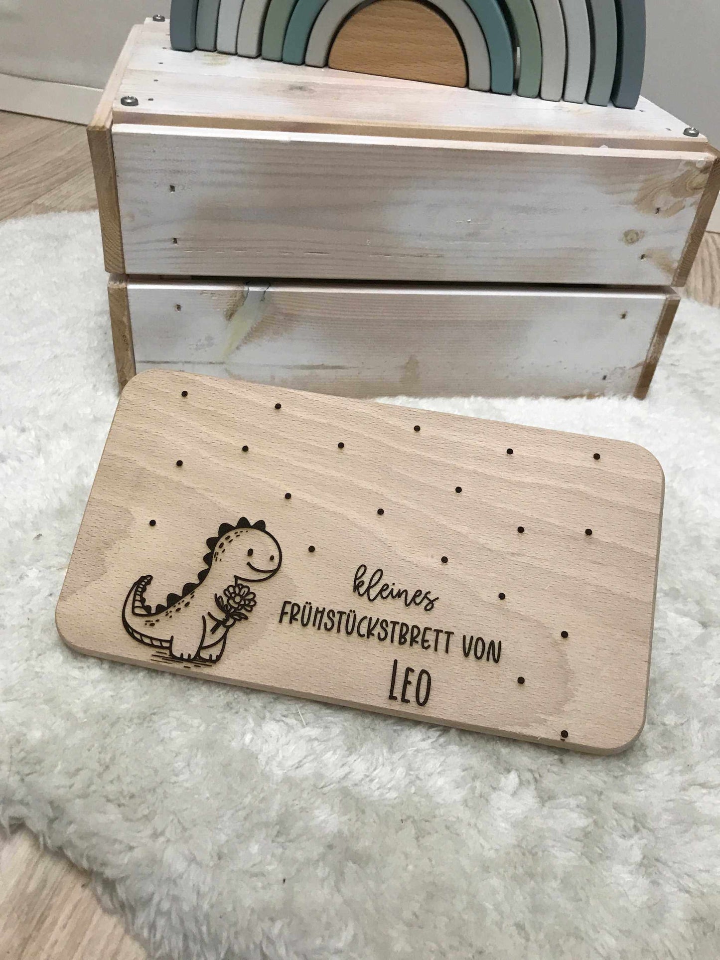 Holz Frühstücksbrettchen mit Dino-Design und personalisierter Gravur auf weißem Teppich.