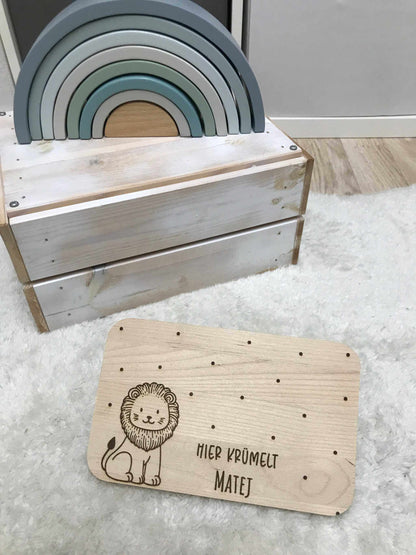 Löwenmotiv Frühstücksbrettchen aus Holz auf weichem Teppich neben Spielzeugbogen.