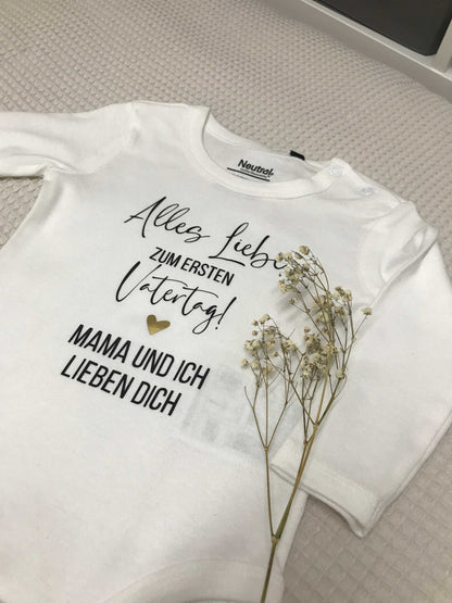 Kuscheliger weißer Babybody mit Text „Alles Liebe zum ersten Vatertag!“ und Blumendekoration, weich und bequem für Babys.