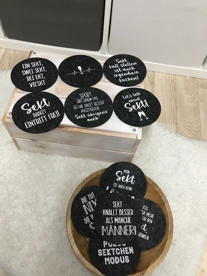Runde Filzuntersetzer mit Sektsprüchen, anthrazitfarbene und hellgraue Varianten, ideales Geschenk für Mädelsabend.