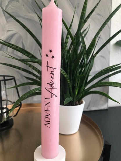 Kerzen in Rosa mit Adventsaufdruck und Pflanzen im Hintergrund.