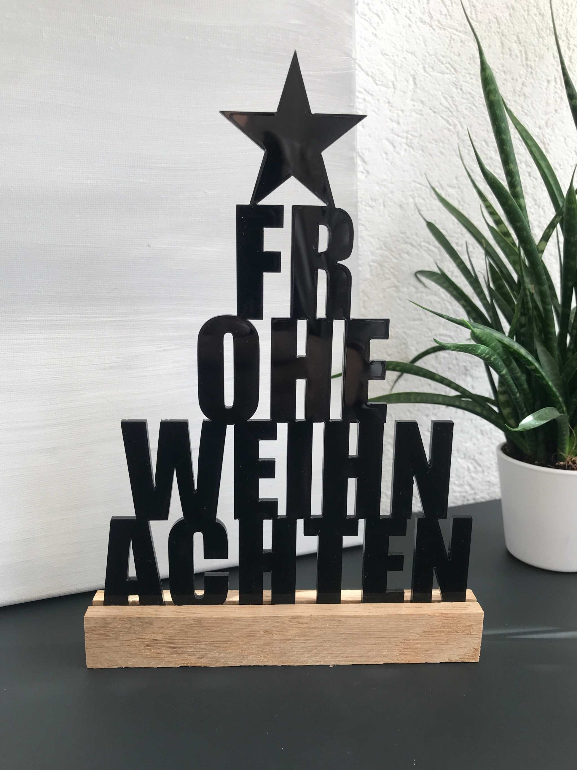 Weihnachtsdekoration aus Acryl und Holz mit "Frohe Weihnachten" Schriftzug auf einem Regal.