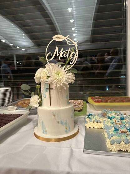 Caketopper Taufe auf zweistöckigem Kuchen mit Blumendekoration und Kreuz, im Hintergrund Buffet.