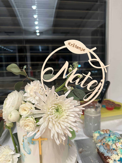 Caketopper aus Holz mit Schriftzug "Matej" und Fischsymbol auf Taufkuchen mit weißen Blumen.