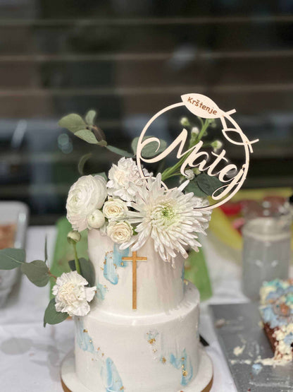 Caketopper für Taufe aus Holz auf zweistöckigem Kuchen mit Blumen und Kreuz-Dekoration.
