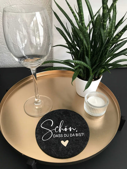 Felt coaster on gold tray with wine glass, candle, and plant, featuring the text "Schön, dass du da bist".