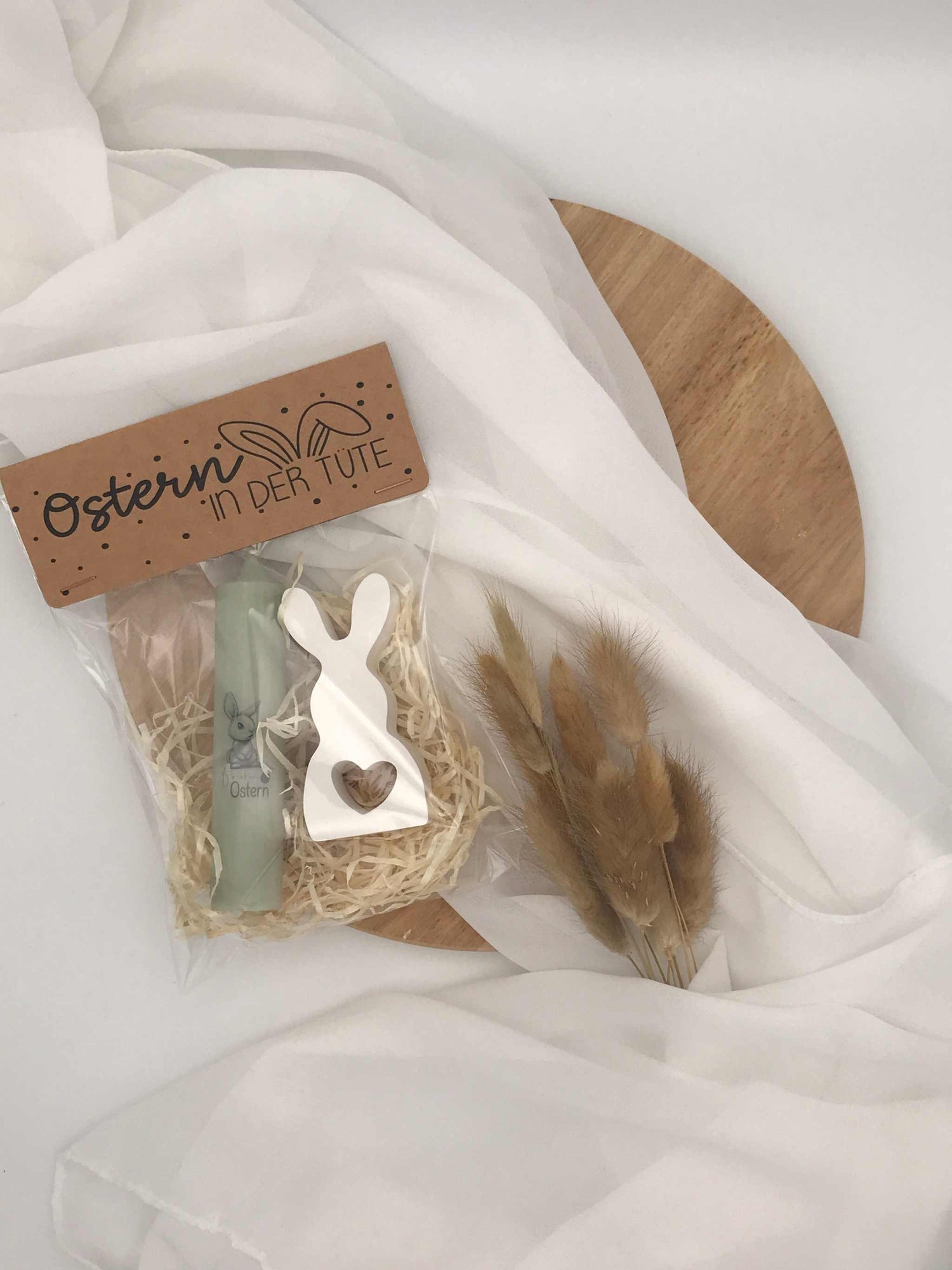 Ostergeschenkset mit Kerze, Raysin Hase und Dekoration in Geschenkverpackung auf Holzplatte.