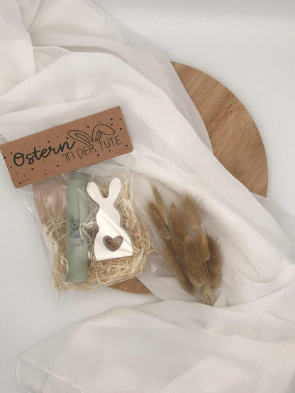 Oster-Geschenkset mit Kerze und Raysin-Hase auf Holzuntergrund, dekoriert mit Trockenblumen.