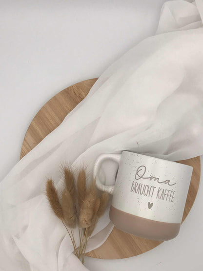 Stylish ceramic coffee mug with "Oma braucht Kaffee" engraving, beige accents, perfect gift.