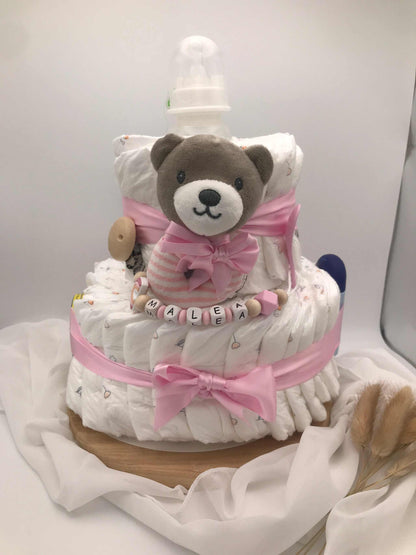 Windeltorte mit Bärchen, rosa Schleife und Schnullerkette auf weißem Hintergrund.