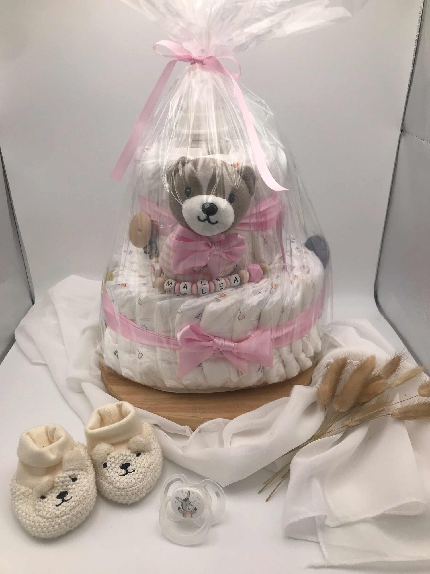 Windeltorte mit Schnullerkette, verpackt in Klarsichtfolie, dekoriert mit Kuscheltier und Schnullerkette, perfektes Geschenk für werdende Eltern.