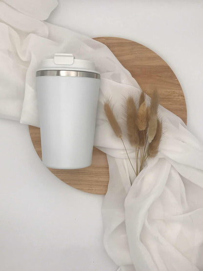 Doppelwandiger Thermobecher mit Gravur, 350 ml, auf Holzunterlage mit weißem Stoff und Trockenblumen.