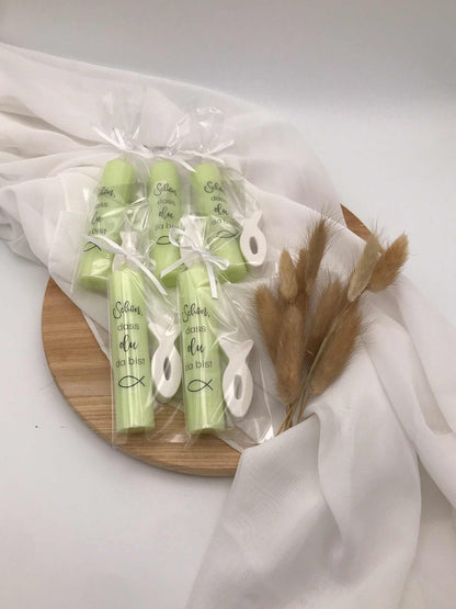 Gastgeschenke zur Taufe mit grünen Kerzen und Fischanhängern auf Holzbrett, dekoriert mit weißem Stoff und Trockenblumen.