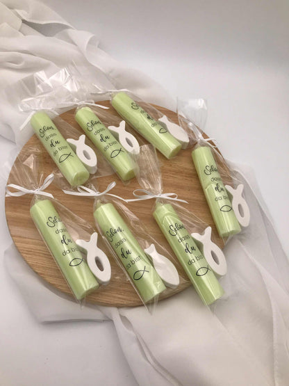Gastgeschenke zur Taufe mit grünen personalisierten Kerzen und symbolischen Fische-Anhängern auf Holzteller.