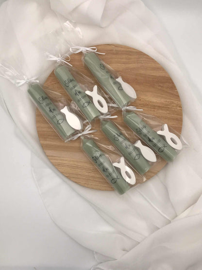 Gastgeschenke zur Taufe oder Kommunion, grüne Kerzen mit Fischanhänger, auf Holzplatte arrangiert.