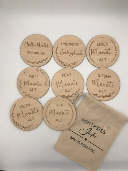 Milestone wooden discs for baby's first year with German inscriptions and a cloth bag.
