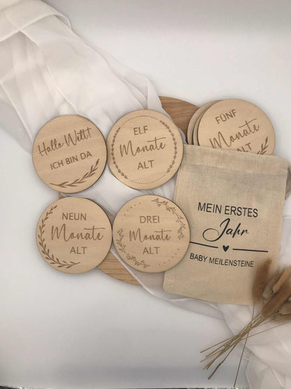 Holzscheiben zur Feier von Babys Meilensteinen im ersten Jahr, mit Gravuren für verschiedene Monate, präsentiert in einem Stoffbeutel.