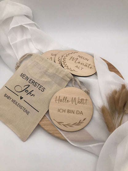Holzscheiben "Meilensteine für Babys erstes Jahr" auf weißem Tuch, mit Lasergravur "Hallo Welt ich bin da". Ideal zum Festhalten besonderer Baby-Momente.