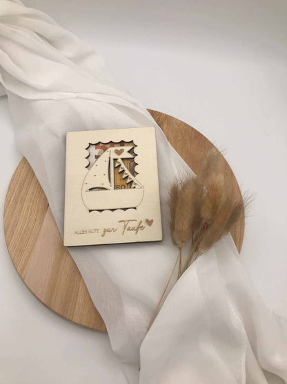 Holzkarte als kreatives Geldgeschenk zur Taufe, auf rundem Holzbrett mit weißem Stoff drapiert.